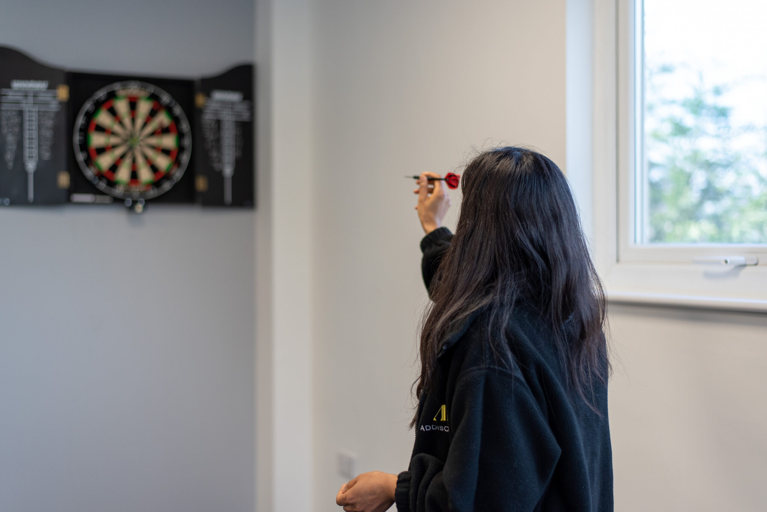 Office games a woman playing darts in an Addison Lee jumper