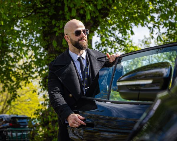 Man wearing sunglasses opening a car door for a passenger