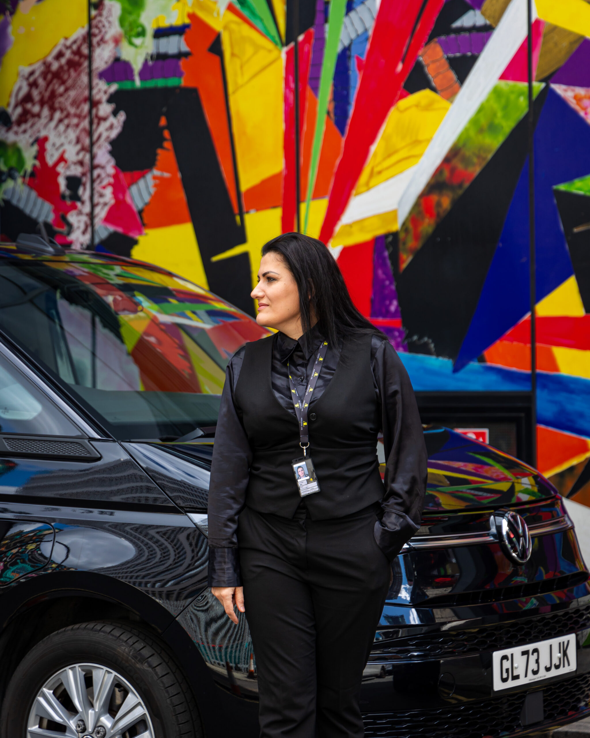 Woman driver stood in front of an Addison Lee by a piece or artwork in Shoreditch