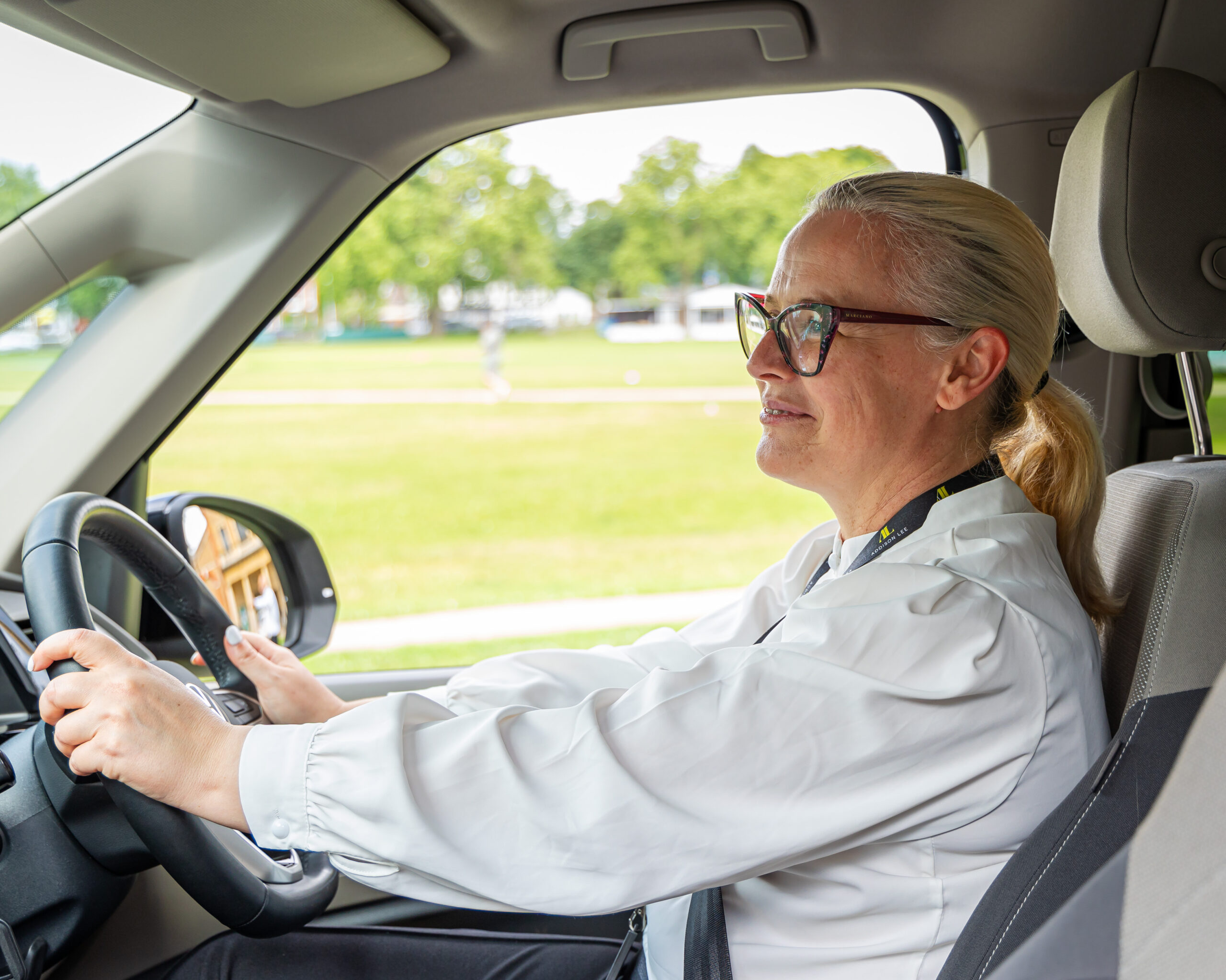 Woman driver wearing glasses and driving an Addison Lee taxi