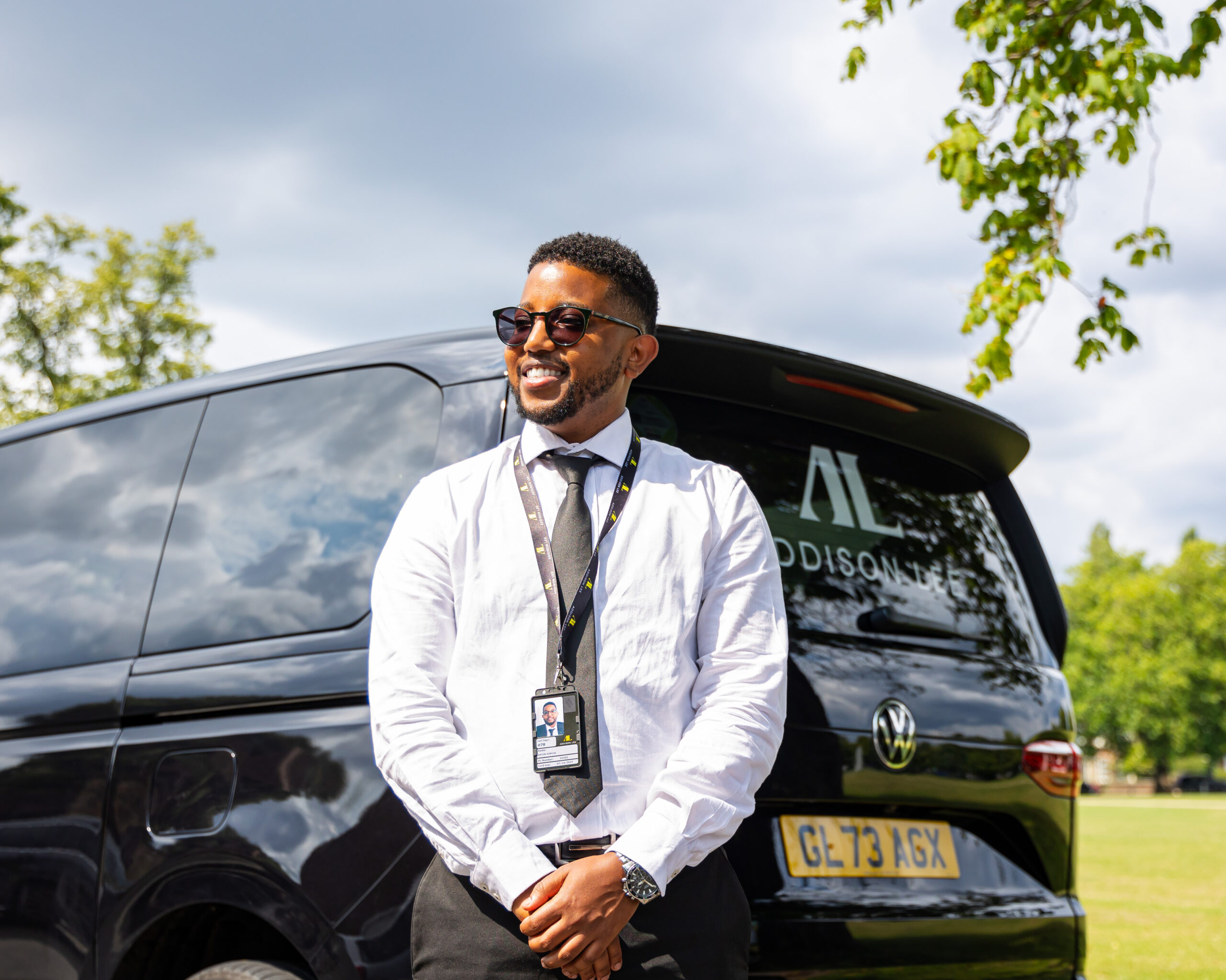 Addison Lee driver stood behind a taxi wearing sunglasses and smiling